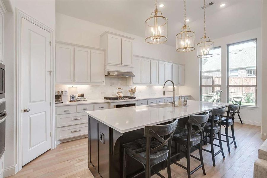 Kitchen featuring pendant lighting, a breakfast bar, white cabinets, a center island with sink, and light wood-type flooring