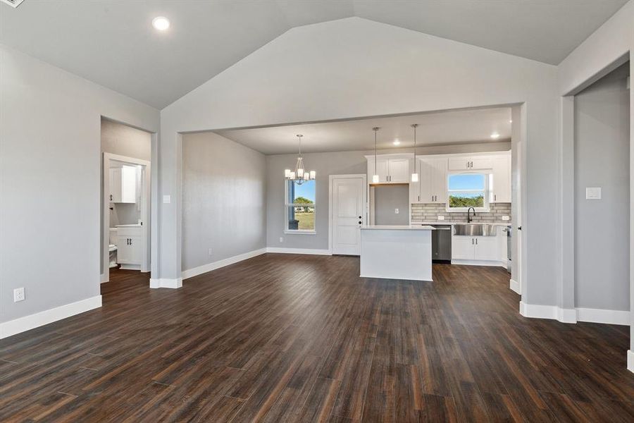 Unfurnished living room with lofted ceiling, sink, dark hardwood / wood-style floors, and a notable chandelier