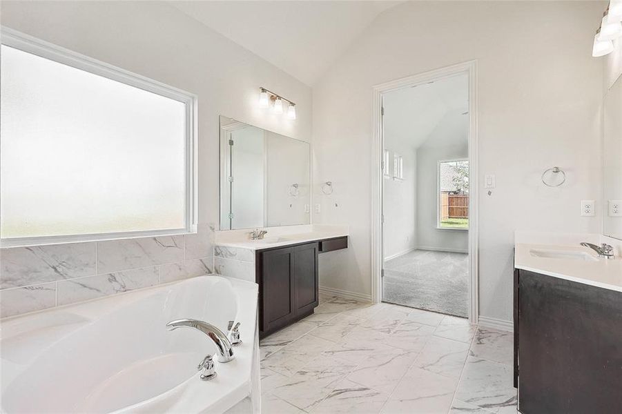 Bathroom featuring dual vanity, tile patterned flooring, lofted ceiling, and a tub