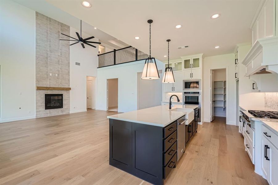 Kitchen featuring ceiling fan, white cabinets, light wood-type flooring, appliances with stainless steel finishes, and a tiled fireplace