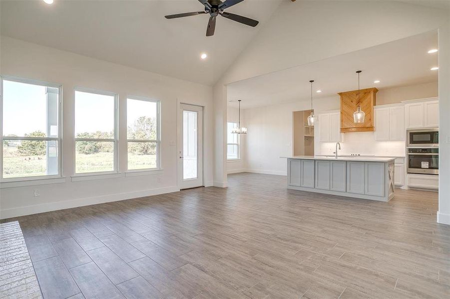 Unfurnished living room with light hardwood / wood-style floors, high vaulted ceiling, sink, and ceiling fan with notable chandelier