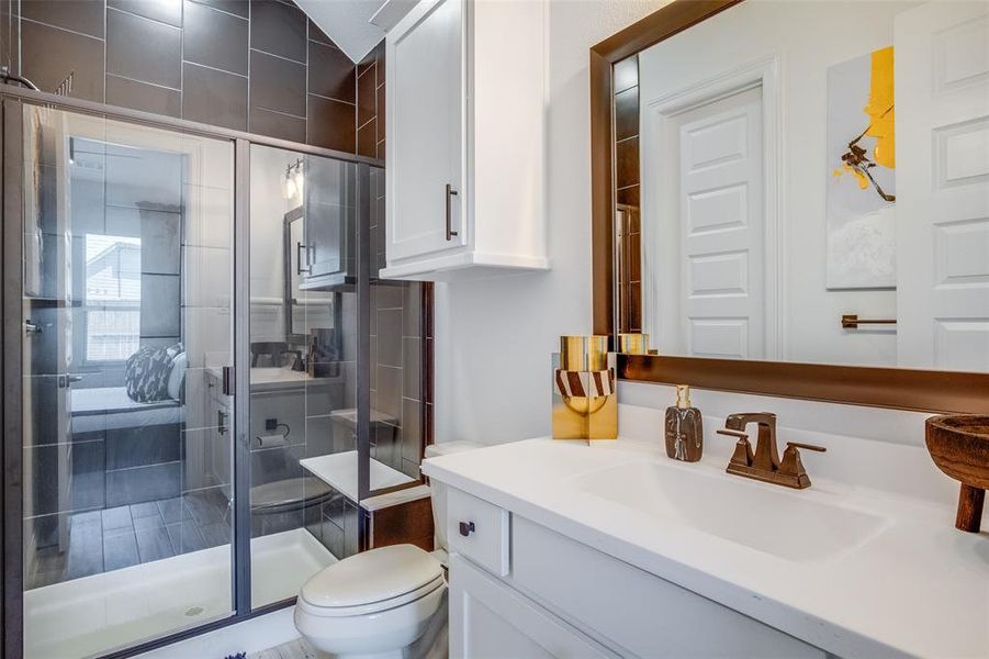 Bathroom featuring a shower with door, toilet, and vanity