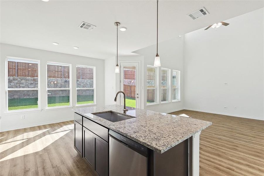 Kitchen with light stone counters, light hardwood / wood-style flooring, dishwasher, a center island with sink, and sink