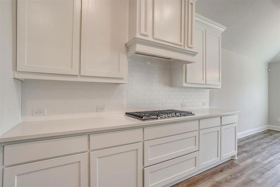 Kitchen featuring custom exhaust hood, white cabinets, decorative backsplash, stainless steel gas stovetop, and light hardwood / wood-style flooring