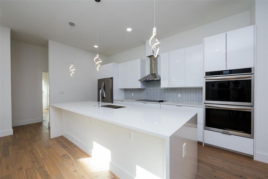 Kitchen featuring light hardwood / wood-style floors, appliances with stainless steel finishes, white cabinets, pendant lighting, and tasteful backsplash
