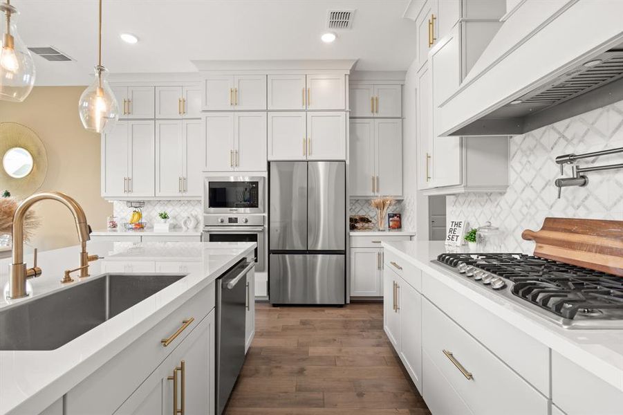 The kitchen boasts stainless steel appliances, complemented by elegant golden fixtures and a convenient pot filler faucet, blending modern functionality with luxurious accents.