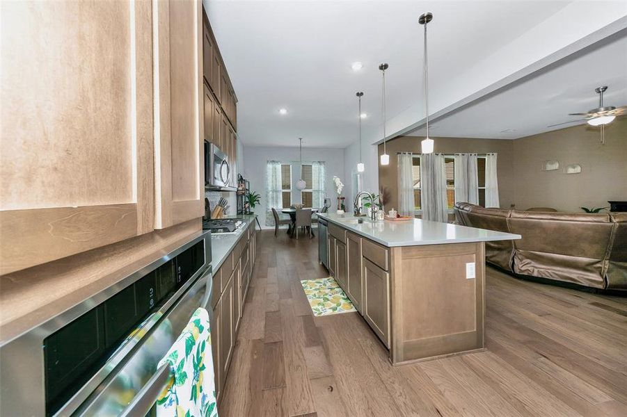 Kitchen with appliances with stainless steel finishes, sink, light wood-type flooring, an island with sink, and pendant lighting