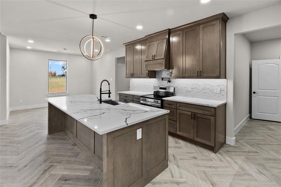 Kitchen featuring light stone counters, sink, a kitchen island with sink, decorative light fixtures, and stainless steel range