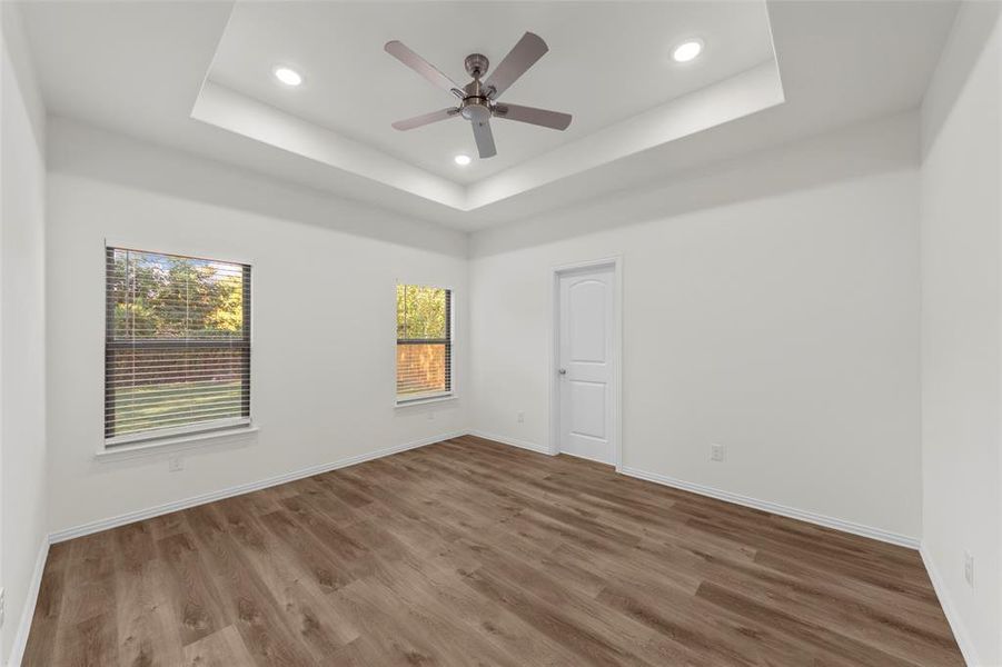 Empty room with a raised ceiling, hardwood / wood-style flooring, and ceiling fan