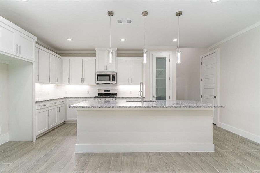 Kitchen with stainless steel appliances, hanging light fixtures, white REAL WOOD cabinets, sink, and a center island with sink