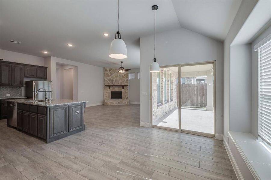 Kitchen with a stone fireplace, hanging light fixtures, dark brown cabinetry, light stone counters, and stainless steel refrigerator