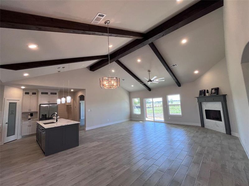 Kitchen with hanging light fixtures, wood-type flooring, a kitchen island with sink, white cabinetry, and stainless steel refrigerator with ice dispenser