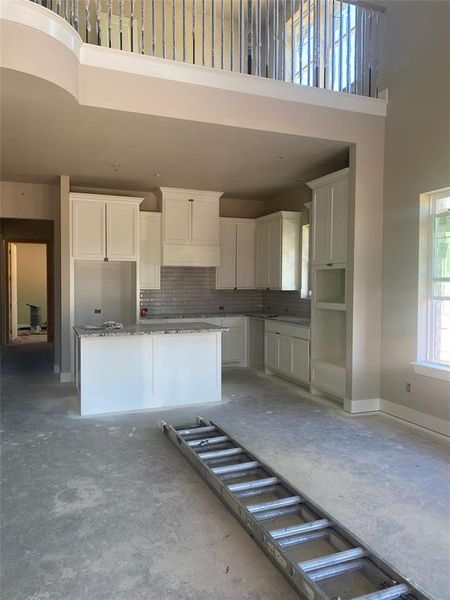 Kitchen with backsplash, stone countertops, white cabinetry, a kitchen island, and a towering ceiling