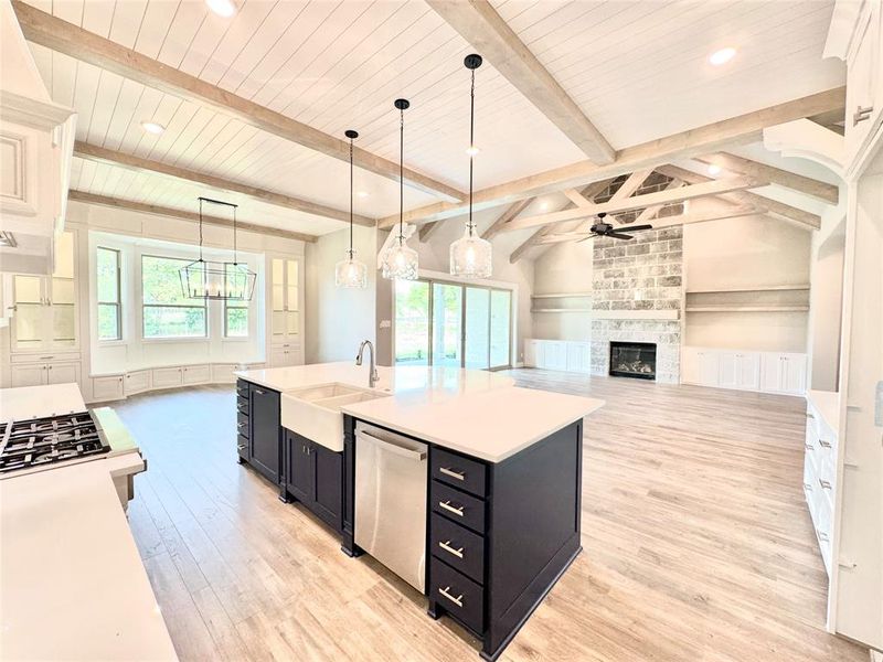 Kitchen featuring ceiling fan with notable chandelier, decorative light fixtures, a fireplace, a kitchen island with sink, and vaulted ceiling with beams