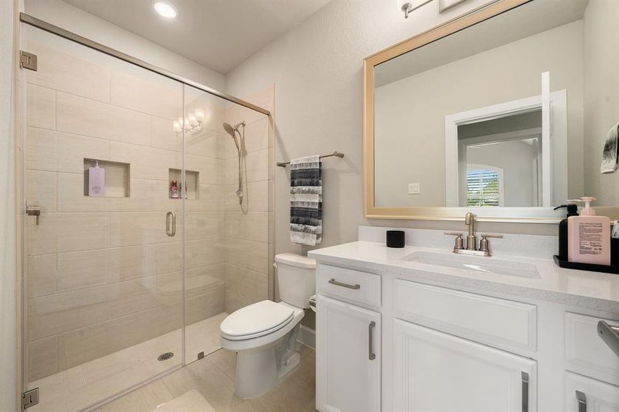 Secondary bathroom features Quartz countertops and bright cabinets, neutral paint, spacious walk in shower with tile surround, large framed mirror, tile floors, sleek fixtures and modern finishes, plenty of space to accommodate any visiting family or guests.