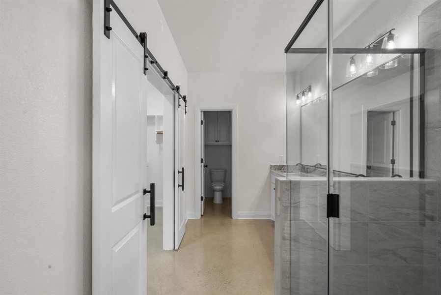 Bathroom with toilet, vanity, concrete floors, and a shower with door