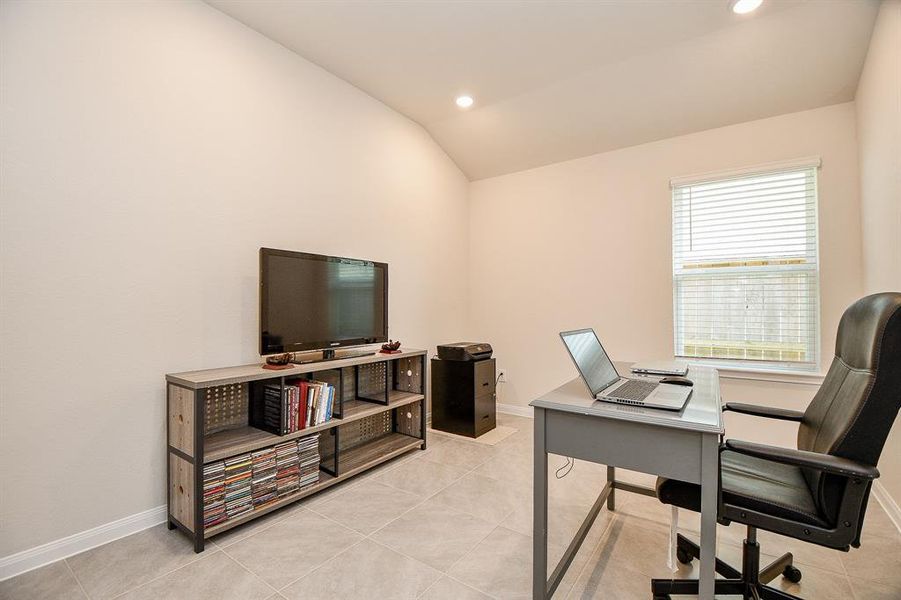 This is a neat and modern home office with tiled flooring, neutral wall colors, and a large window providing natural light.