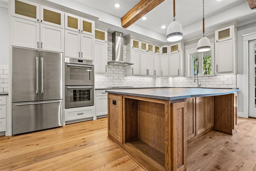 Thermador appliances!  Kitchen with a kitchen island, beam ceiling, light hardwood / wood-style floors, high end stainless steel appliances, and wall chimney range hood custom cabinets