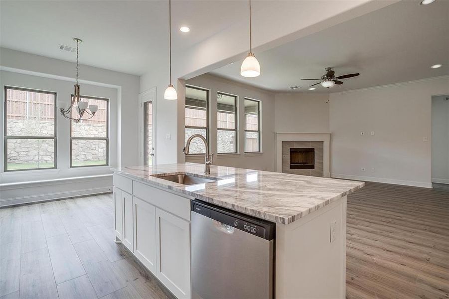 Kitchen featuring light wood-type flooring, white cabinets, stainless steel dishwasher, a tile fireplace, and sink