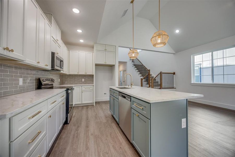 Kitchen featuring sink, stainless steel appliances, an island with sink, decorative light fixtures, and light wood-type flooring