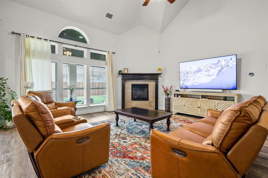 Living room featuring light wood-type flooring, a tile fireplace, ceiling fan, and high vaulted ceiling