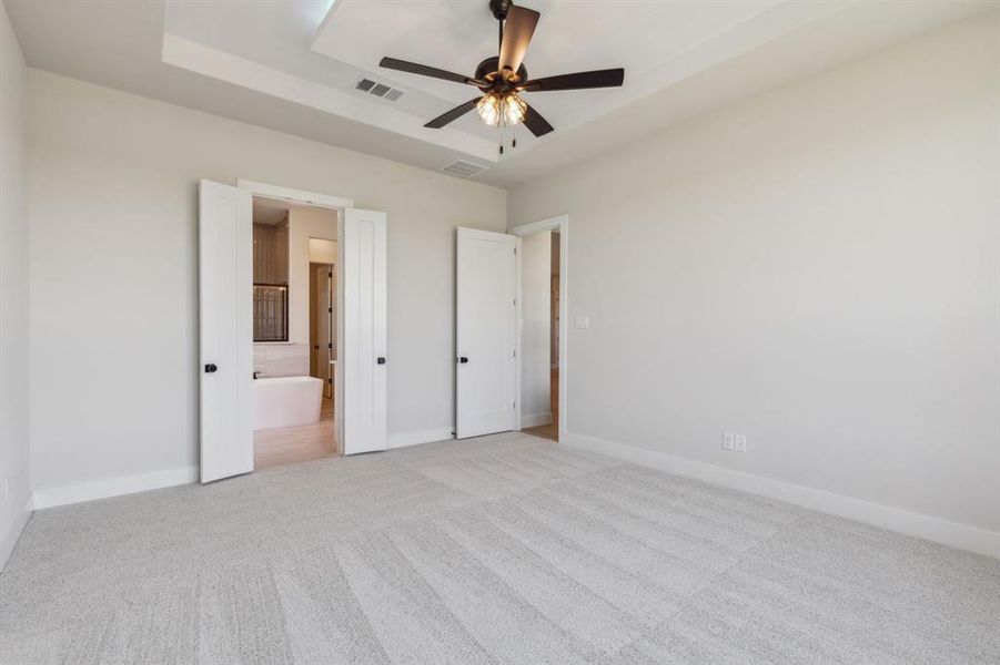 Unfurnished bedroom featuring light carpet, ensuite bath, and ceiling fan