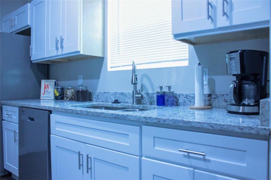 Kitchen with light stone countertops, sink, dishwasher, and white cabinets