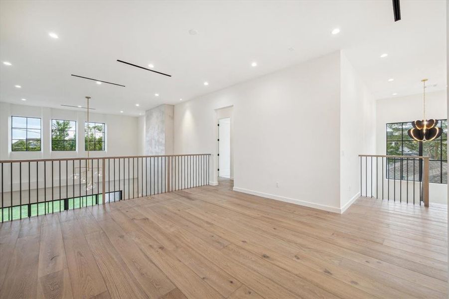 Spacious second floor landing gameroom with hardwood floors, recessed lighting, and a sleek modern railing overlooking the living space. Ample natural light pours in through large windows, making this area perfect for a lounge space.