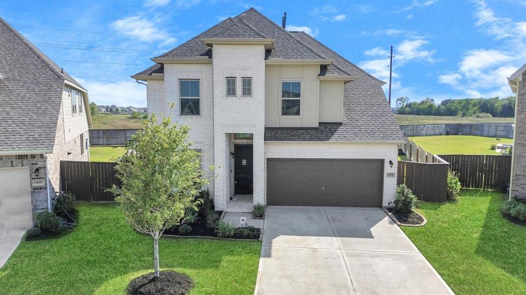 This is a two-story, modern home with a brick facade, featuring a two-car garage and a neatly landscaped front yard. The property includes a fenced backyard with ample green space, situated in a residential neighborhood.