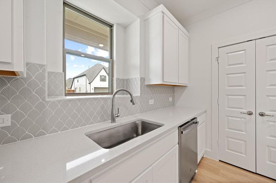 Kitchen with white cabinetry, tasteful backsplash, dishwasher, light hardwood / wood-style floors, and sink