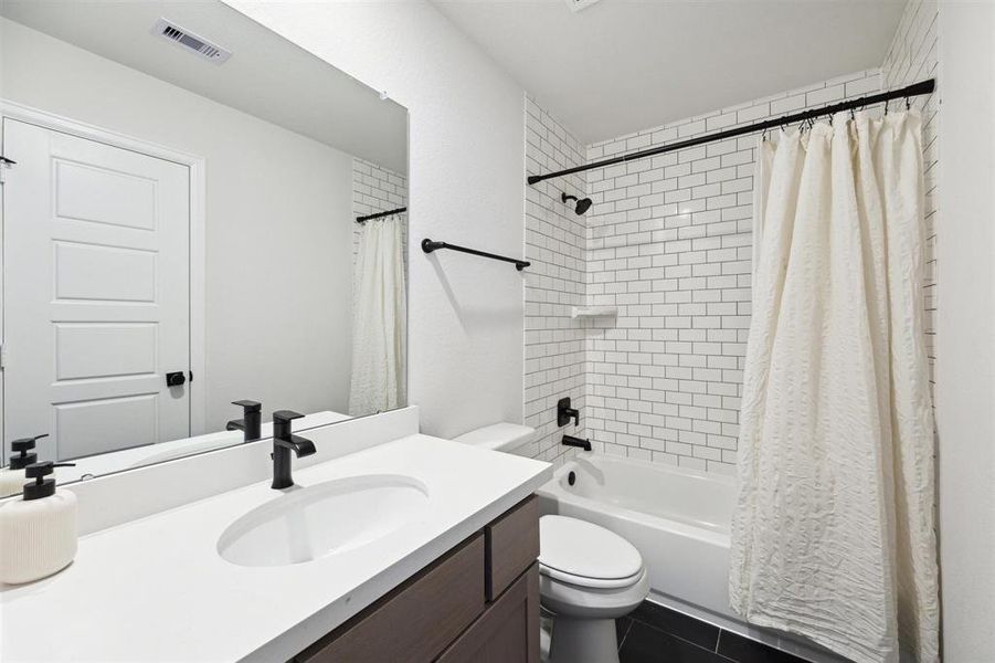 The secondary bathroom upstairs features clean-lines and a white subway tile shower with tub, a sleek vanity with a large mirror, and contemporary black fixtures.