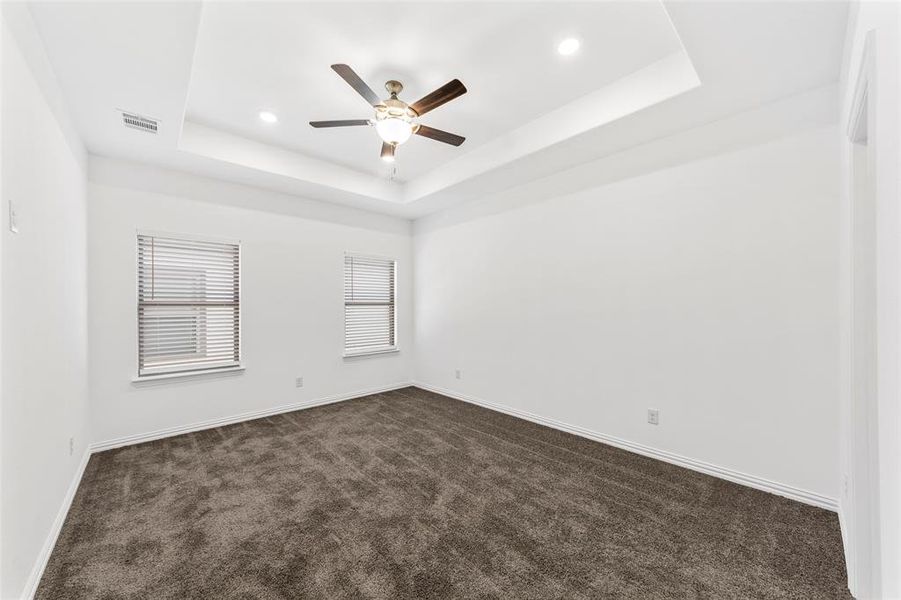 Empty room featuring ceiling fan, a raised ceiling, and dark carpet