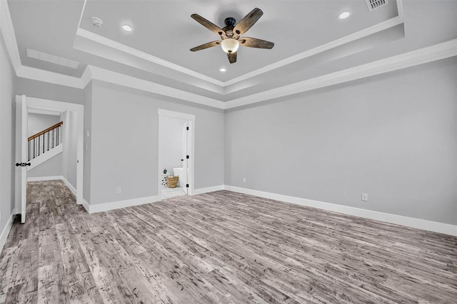 Empty room with ornamental molding, light hardwood / wood-style floors, ceiling fan, and a raised ceiling