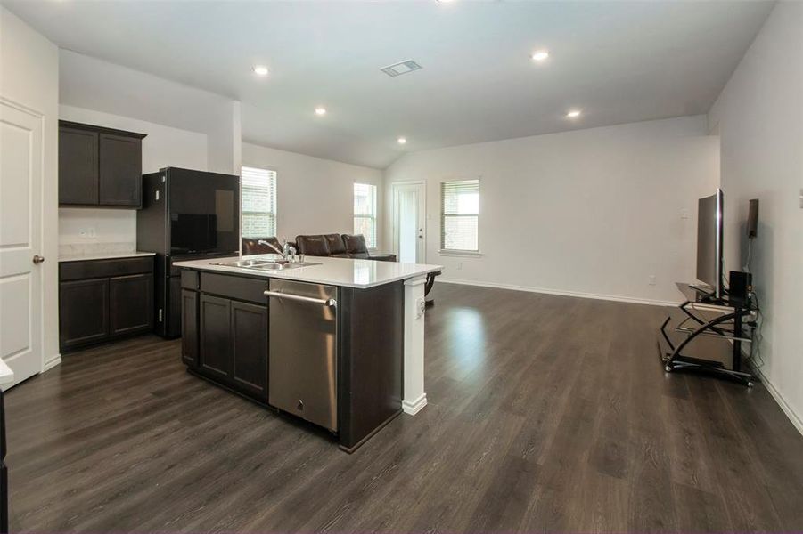 Kitchen with dark hardwood / wood-style floors, dishwasher, vaulted ceiling, and a center island with sink
