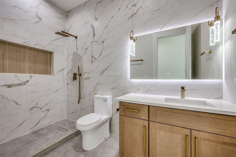 Bathroom featuring vanity, a tile shower, tile walls, and toilet