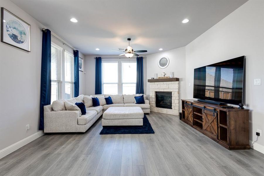 Living room featuring ceiling fan, a stone fireplace, and light hardwood / wood-style floors