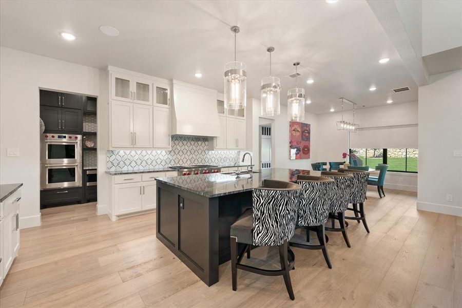 Kitchen featuring a center island with sink, premium range hood, white cabinets, light wood-type flooring, and double oven