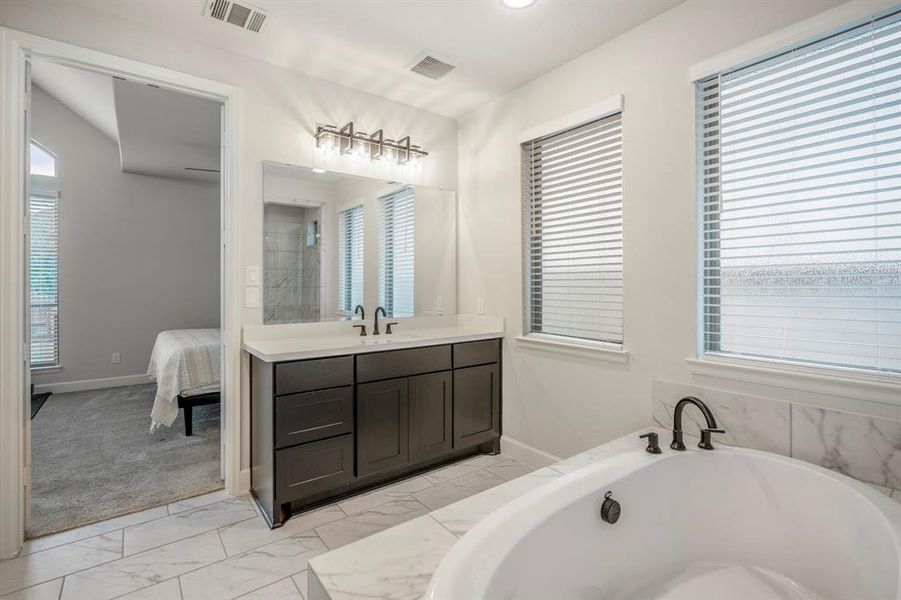 The primary bathroom features two separate large vanity areas with separate sinks, quartz countertops, plenty of cabinet space, a large mirror, and overhead lighting.