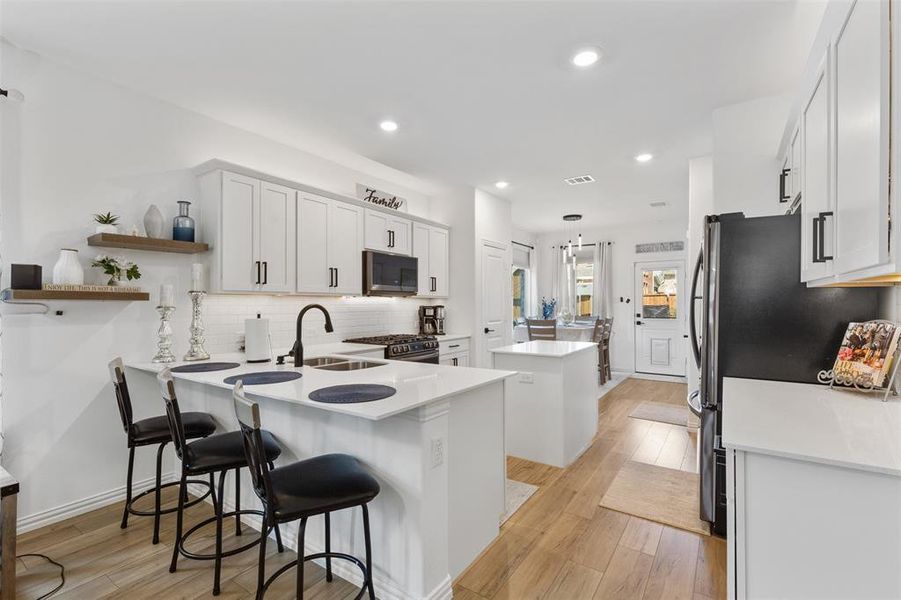 Kitchen featuring light hardwood / wood-style floors, white cabinets, kitchen peninsula, a breakfast bar area, and stainless steel appliances