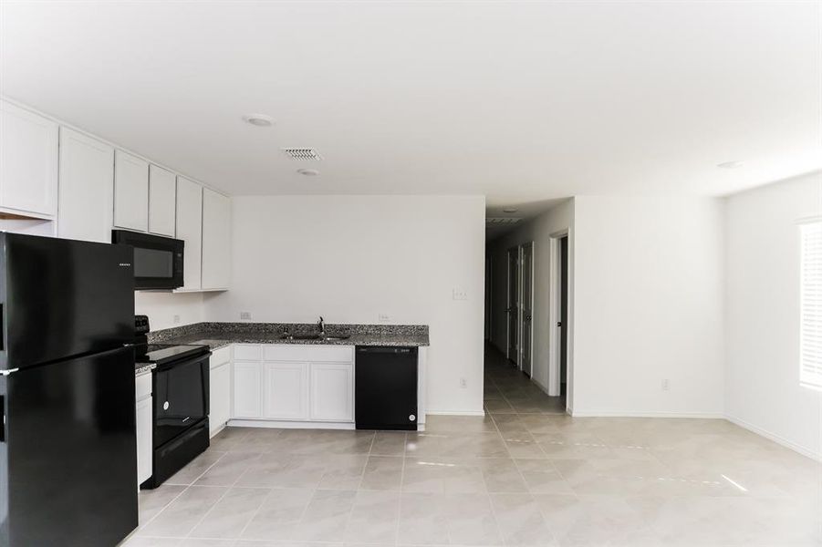 Kitchen featuring black appliances, white cabinetry, sink, and light tile patterned floors