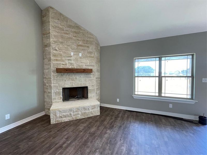 Unfurnished living room with a stone fireplace, lofted ceiling, and dark hardwood / wood-style flooring