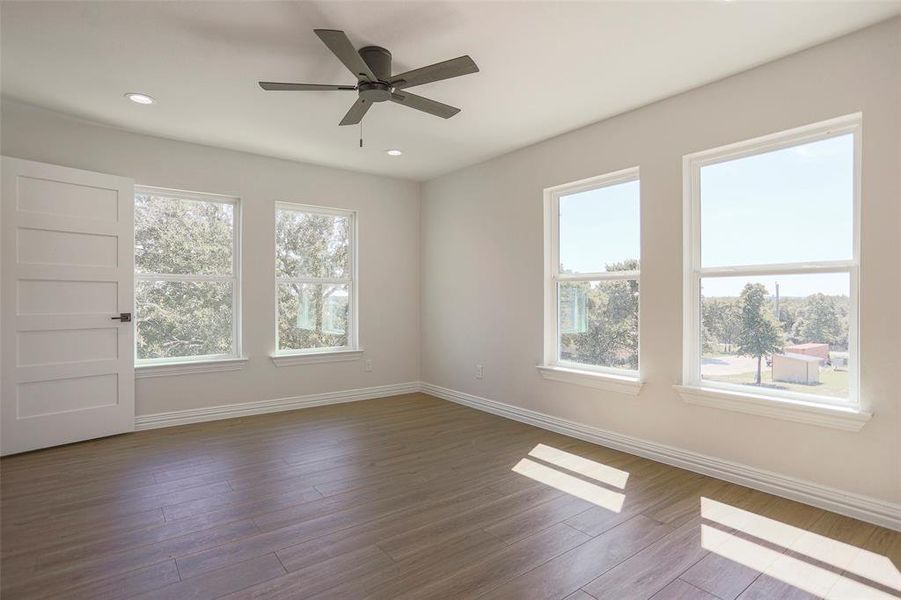 Empty room with ceiling fan, dark hardwood / wood-style flooring, and a healthy amount of sunlight