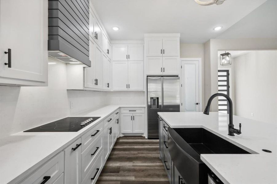 Kitchen with white cabinets, dark wood-type flooring, black electric stovetop, and custom exhaust hood