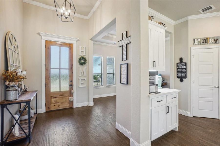 Entrance foyer with crown molding, dark wood-type flooring, and a notable chandelier