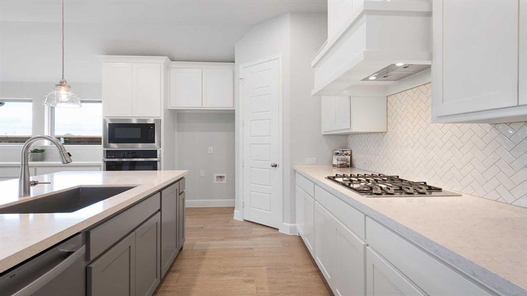 Kitchen with white cabinets, decorative light fixtures, appliances with stainless steel finishes, custom exhaust hood, and sink