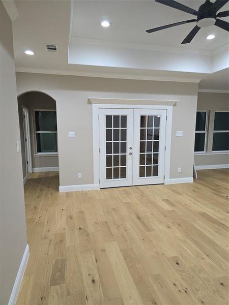 Unfurnished living room featuring light hardwood / wood-style flooring, a raised ceiling, crown molding, ceiling fan, and french doors