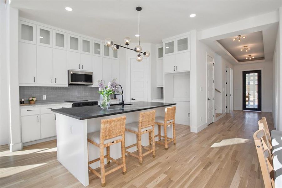 Kitchen with tasteful backsplash, light hardwood / wood-style flooring, a notable chandelier, white cabinets, and an island with sink