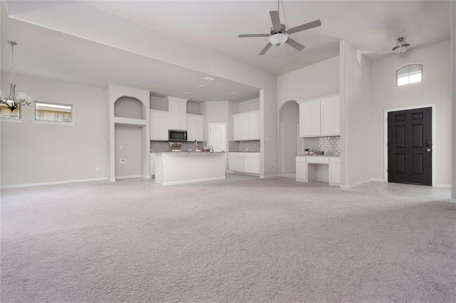 Unfurnished living room featuring a high ceiling, light carpet, and ceiling fan with notable chandelier