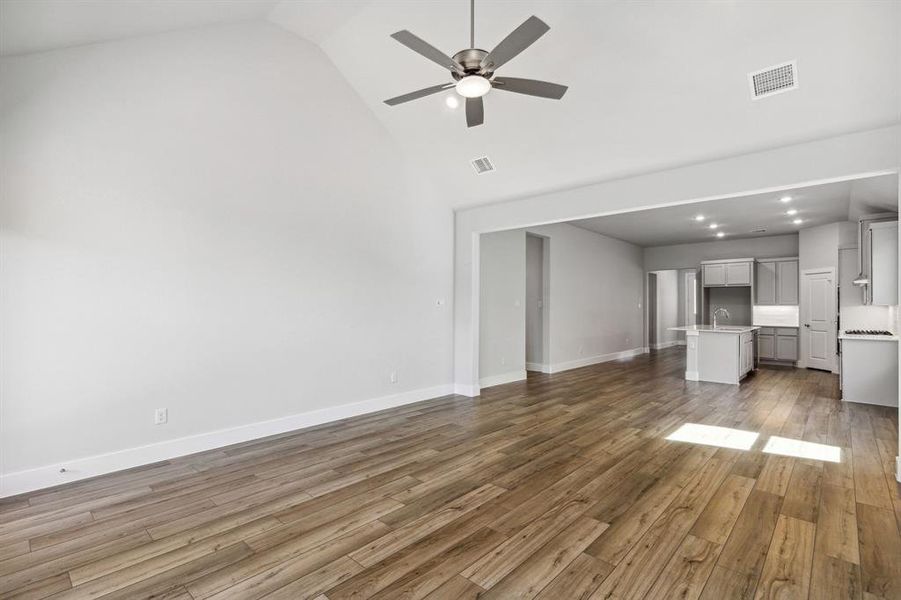 Unfurnished living room with hardwood / wood-style floors, vaulted ceiling, and ceiling fan