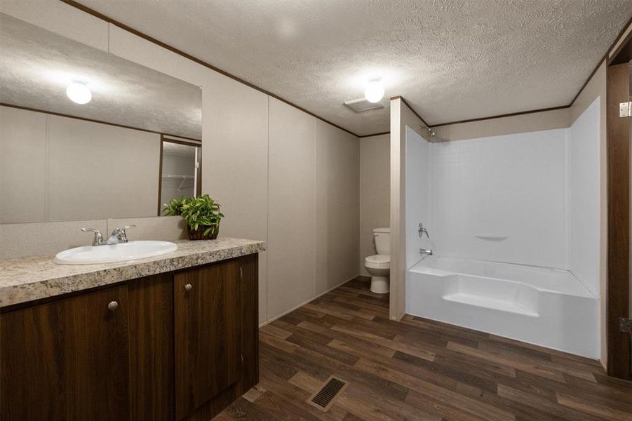 Full bathroom with hardwood / wood-style floors, a textured ceiling, shower / bath combination, toilet, and vanity